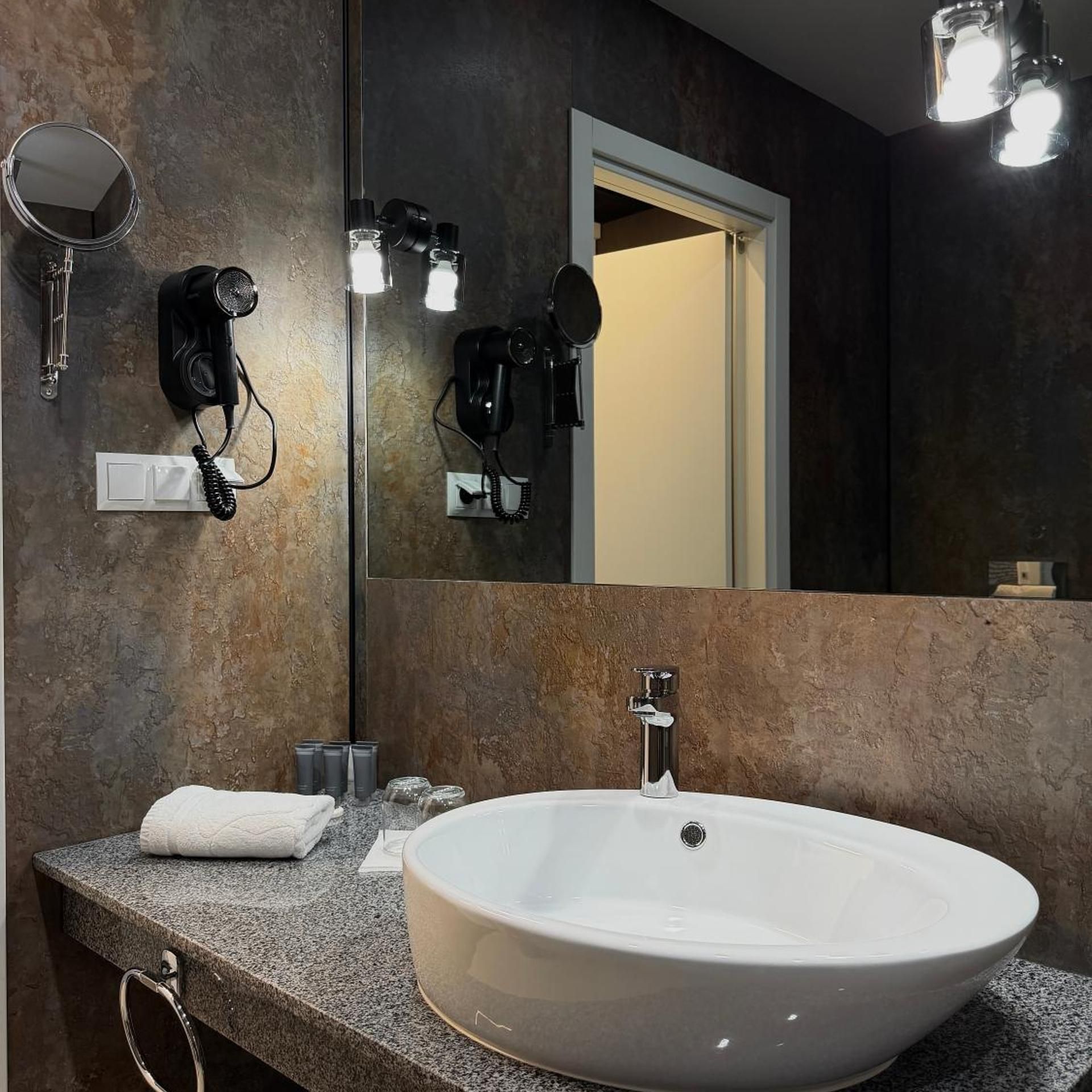 Ein Badezimmer mit einem großen, weißen Waschbecken, einem Spiegel und zwei an der Wand befestigten Haartrocknern.