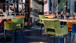 A restaurant interior with brick walls, large windows, and green upholstered chairs. - Hotel Alhar (Lubliniec)