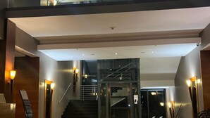 A spacious lobby with a glass elevator, a staircase, and a polished marble floor. - Hotel Alhar (Lubliniec)