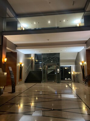 A spacious lobby with a glass elevator, a staircase, and a polished marble floor. - Alhar (Lubliniec)