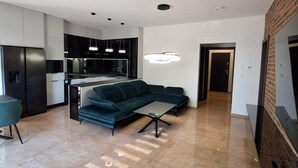 A modern kitchen with black cabinets and stainless steel appliances, a green sofa, and a dining table. - Hotel Alhar (Lubliniec)