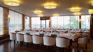 A large dining area with round tables set for multiple guests, featuring white chairs and a wooden floor. - Hotel Alhar (Lubliniec)