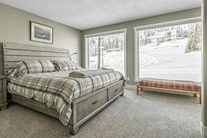 Une chambre à coucher avec un lit, un banc et une fenêtre donnant sur un paysage enneigé.