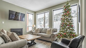 Un salon chaleureux avec une cheminée, une grande fenêtre donnant sur un paysage enneigé et un sapin de Noël.
