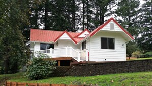 Une maison à deux étages, avec un toit rouge et une façade blanche, dotée d’un porche à l’avant et d’une petite terrasse.