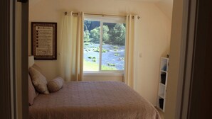 Une chambre à coucher avec un lit, une fenêtre donnant sur une rivière et un texte encadré accroché au mur.