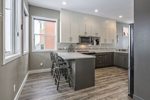 A modern kitchen with grey cabinets, a central island with bar stools, a microwave, and a refrigerator.