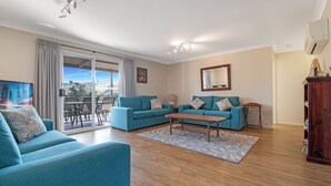 Un salón con dos sofás azules, una mesa de centro de madera y un ventanal con vistas al exterior.