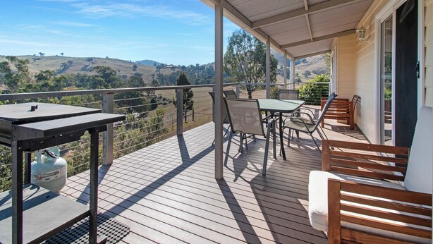Una terraza de madera con una mesa y sillas, con vistas a un paisaje montañoso.