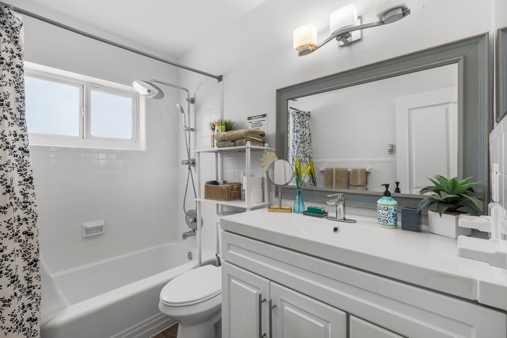 Un baño moderno con bañera, inodoro y lavamanos. Hay una ventana con vistas al exterior, un espejo y diversos artículos de aseo en la encimera.