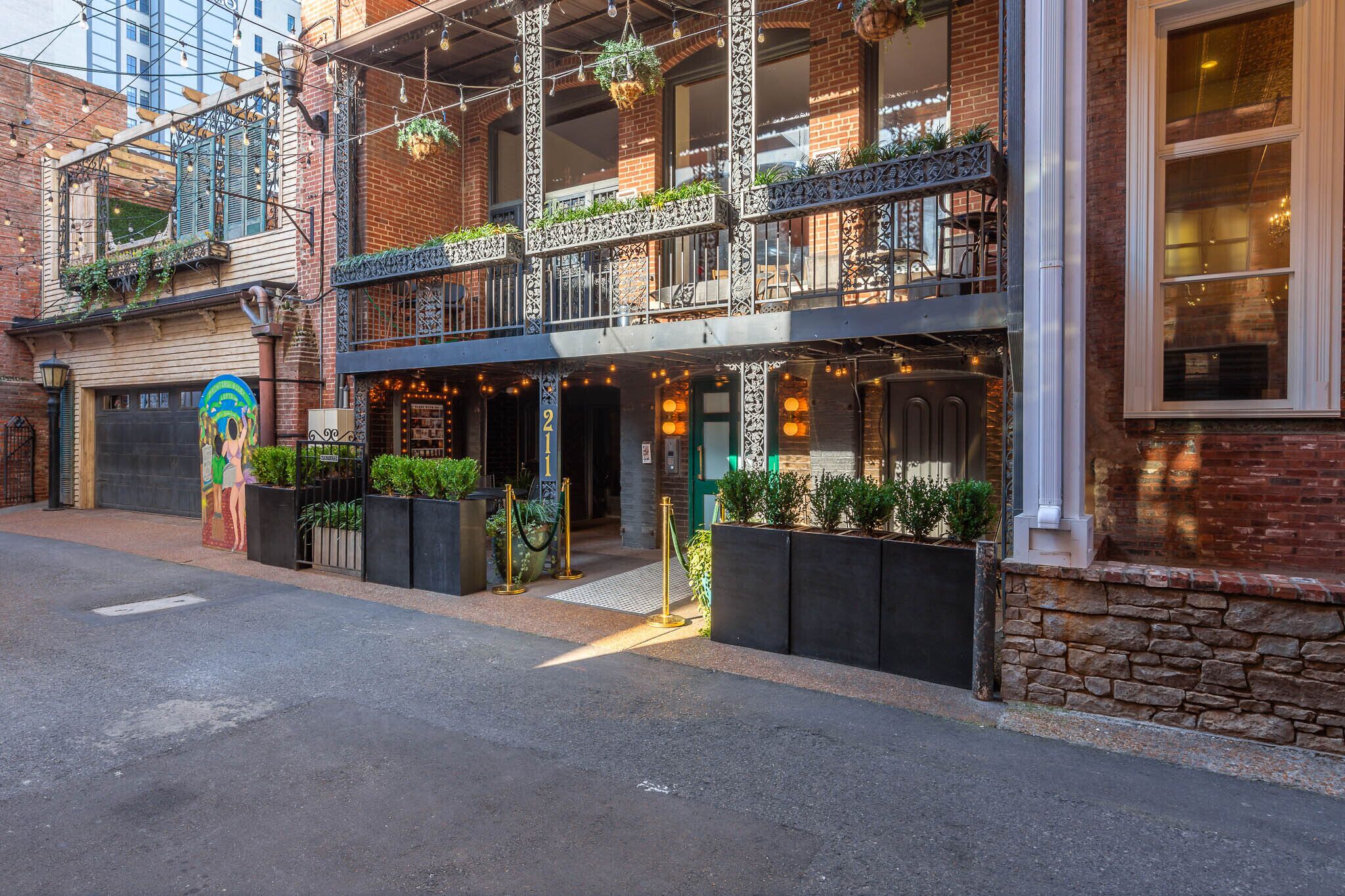 A multi-story building with a brick facade, outdoor seating area with string lights, and a mural on the ground floor.