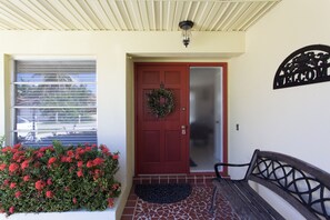 A red door with a wreath, a bench, and a welcome sign on the wall.