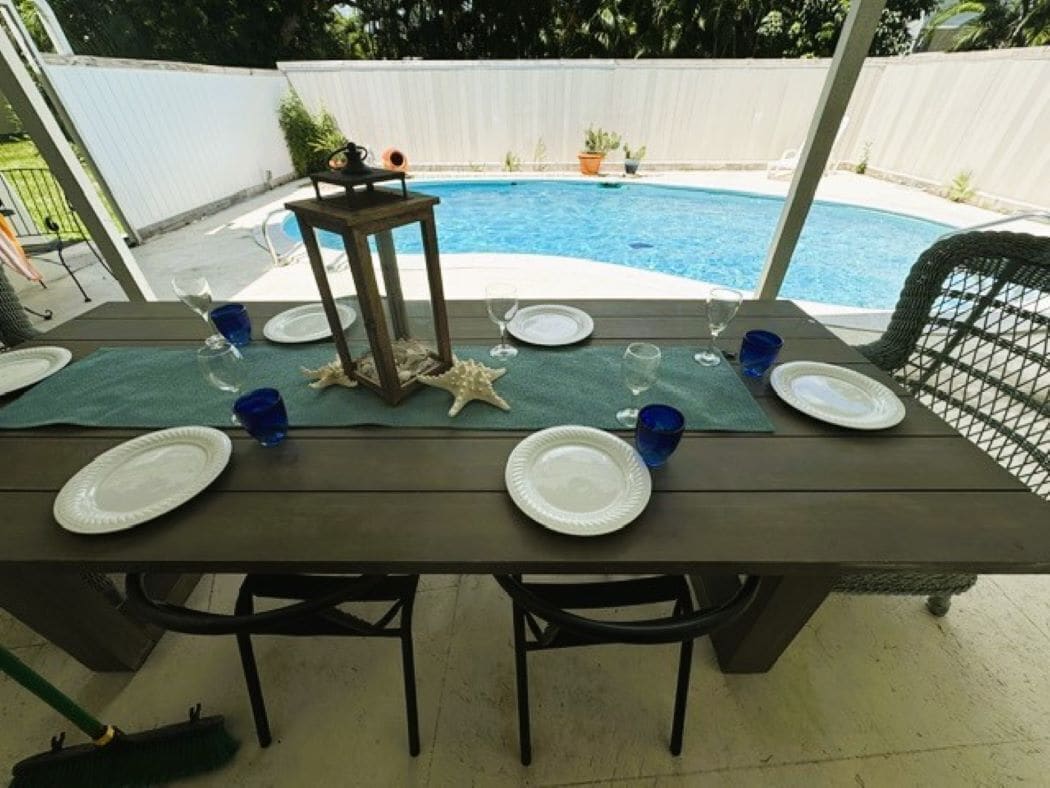 An outdoor dining table set with plates, glasses, and a starfish decoration, overlooking a swimming pool.