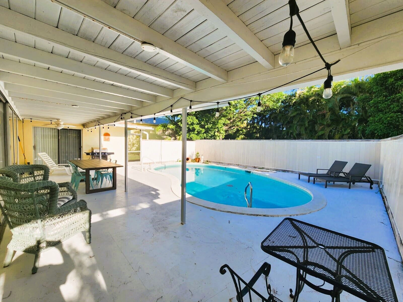 An outdoor pool area with a covered patio, lounge chairs, and a table.