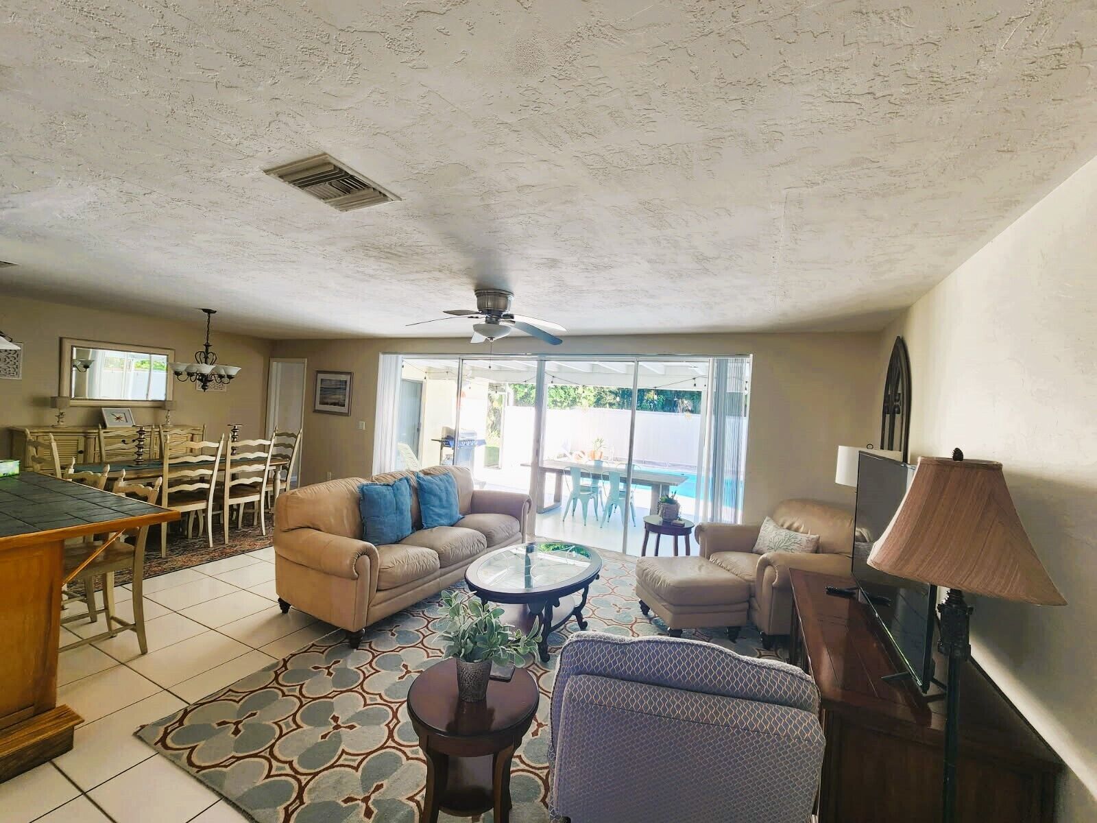 A spacious living room with a dining area, a ceiling fan, and a view of a pool through large glass doors.