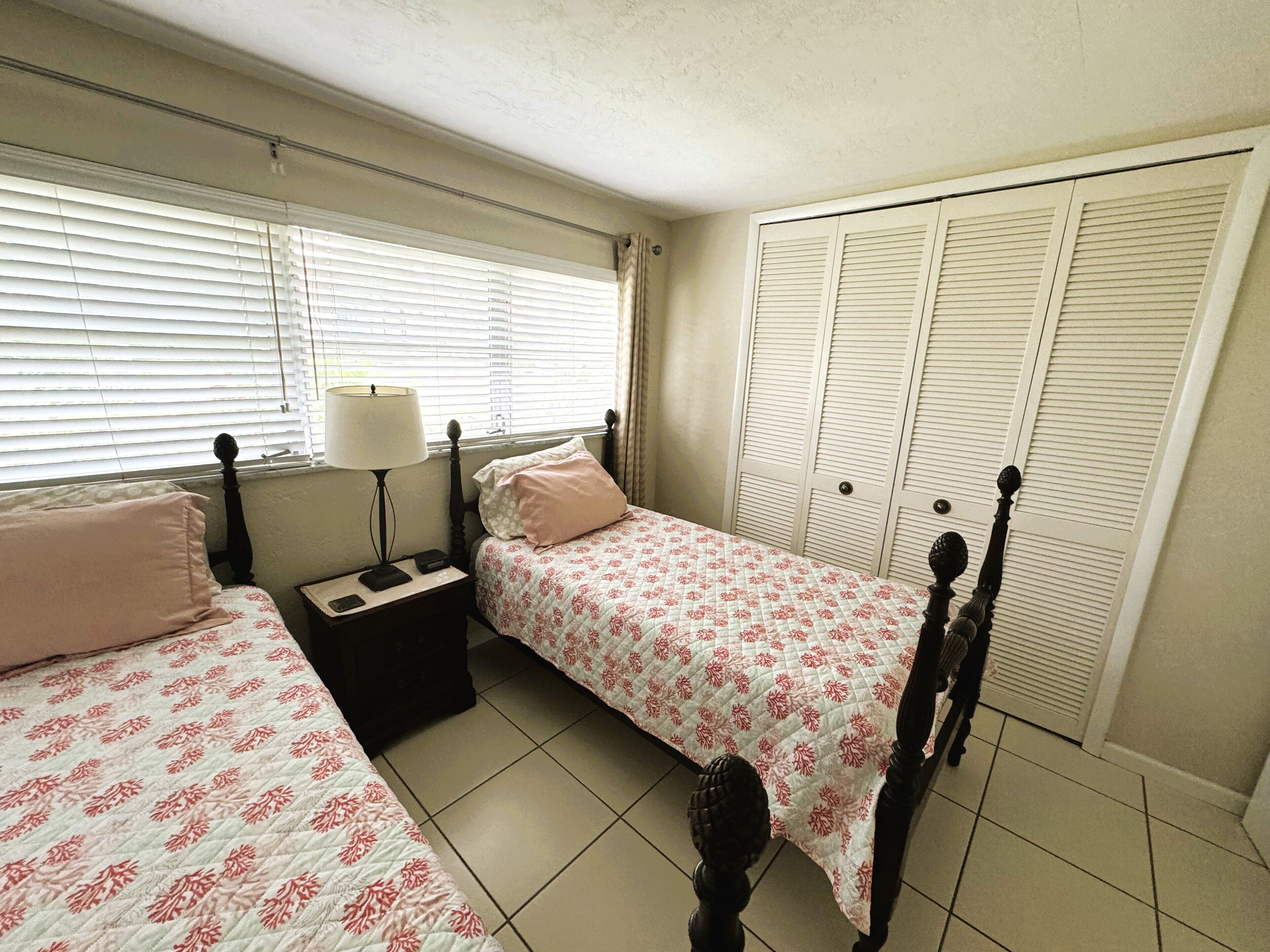 A bedroom with two beds, a nightstand, a lamp, and a closet.