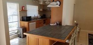 A kitchen with wooden cabinets, a microwave, a sink, and a clock on the wall.
