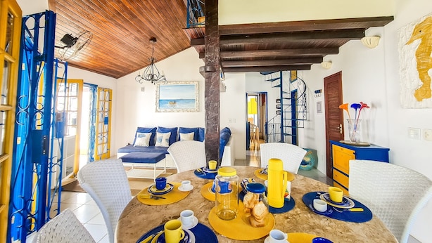 Un coin repas avec une table ronde dressée pour quatre personnes, agrémenté de vaisselle jaune et bleue.