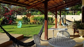 A covered patio with a table and chairs, a hammock, and a garden with a lawn and potted plants.