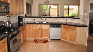 A kitchen with wooden cabinets, a black countertop, a stainless steel refrigerator, and a dishwasher. - Your Backyard Oasis Waiting ..., beautiful home in an award winning community (Gilbert)