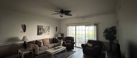 A living room with a ceiling fan, a sofa set, a coffee table, and a TV.