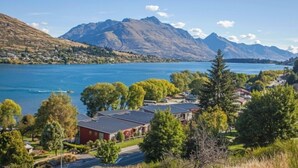 Une propriété située au bord d’un lac, avec une vue sur les montagnes, comprenant un bâtiment rouge et une végétation luxuriante.