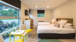 Une chambre moderne avec deux lits, un petit bureau et une fenêtre donnant sur un paysage verdoyant.