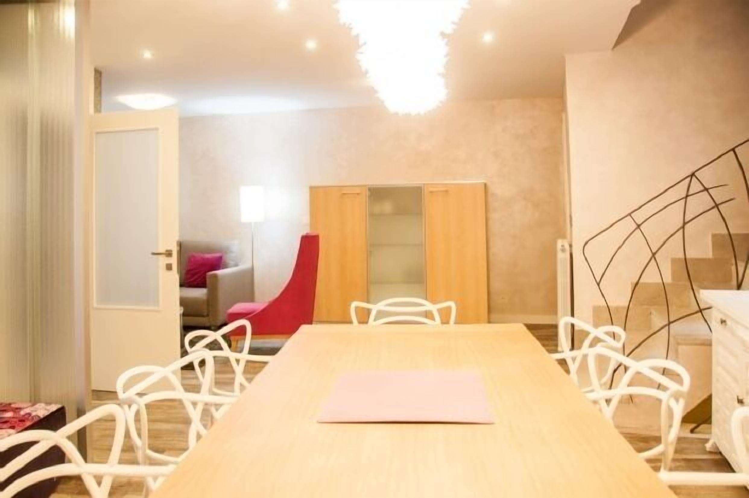 A modern room with a wooden dining table, white chairs, a red chair, a wardrobe, and a staircase.
