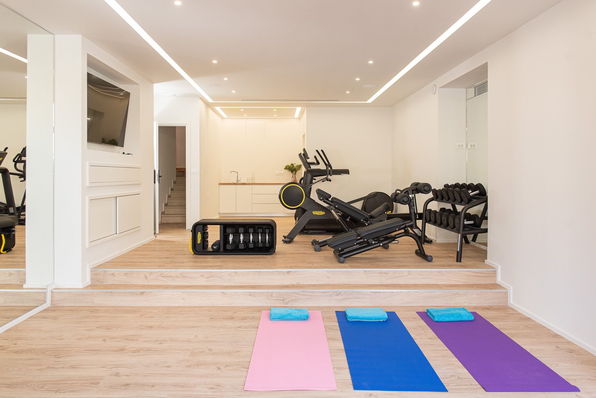A home gym with exercise equipment, yoga mats, and a staircase leading to another room.