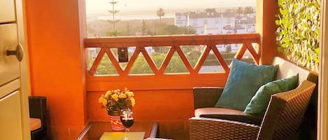 A balcony with wicker furniture, a table with a glass of wine, and potted plants.