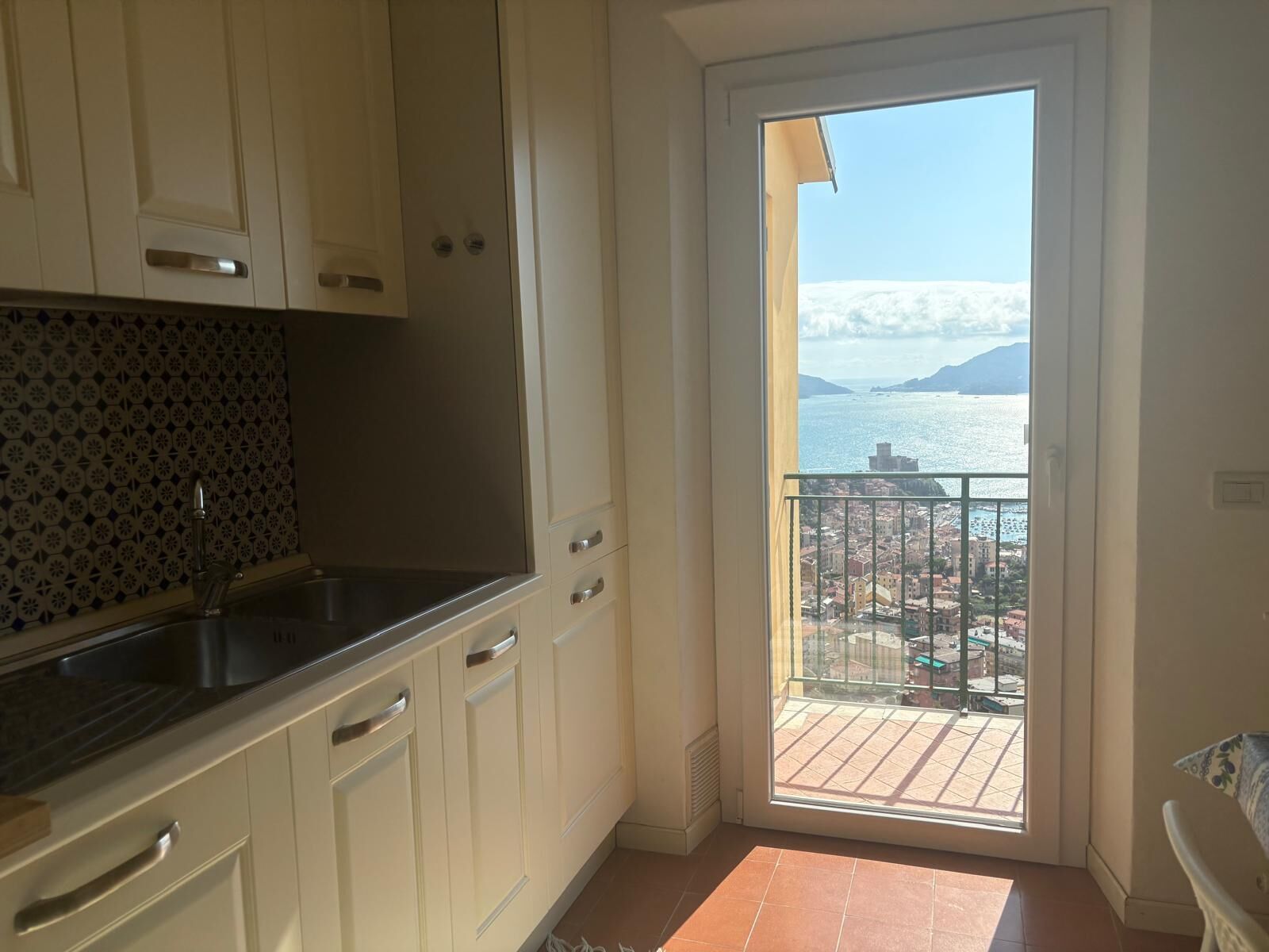 A kitchen with white cabinets, a black countertop, and a view of a balcony with a cityscape and mountains in the background.