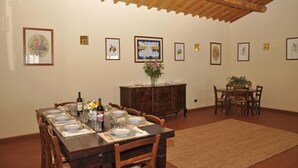 A dining area with a wooden table set for four, surrounded by chairs. There are framed botanical prints on the walls, a wooden cabinet, and a potted plant on the table. - Luxury Villa for 16 with Private Pool near Rome - Santa Cristina Estate (Magliano Sabina)