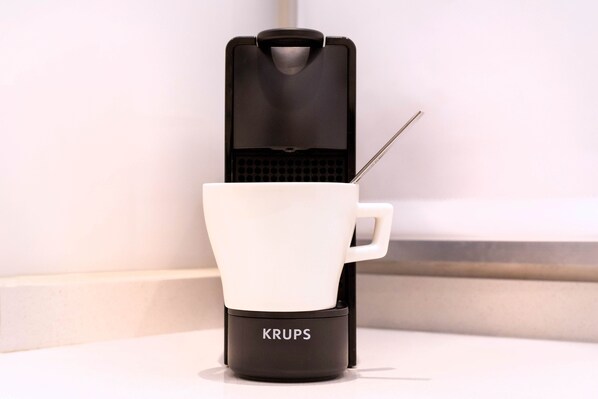 Eine Kaffeemaschine mit Tasse und Löffel, beschriftet mit „KRUPS“, steht auf einer Oberfläche.