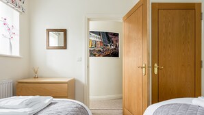 A bedroom with two beds, a wooden wardrobe, a framed picture on the wall, and a window with a vase of flowers. - Luxury 2BR apartment 500m from beach and close proximity to New Forest  (Boscombe, Bournemouth)