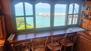 Una cucina rustica con un'ampia finestra che si affaccia su una costa rocciosa e un mare turchese.