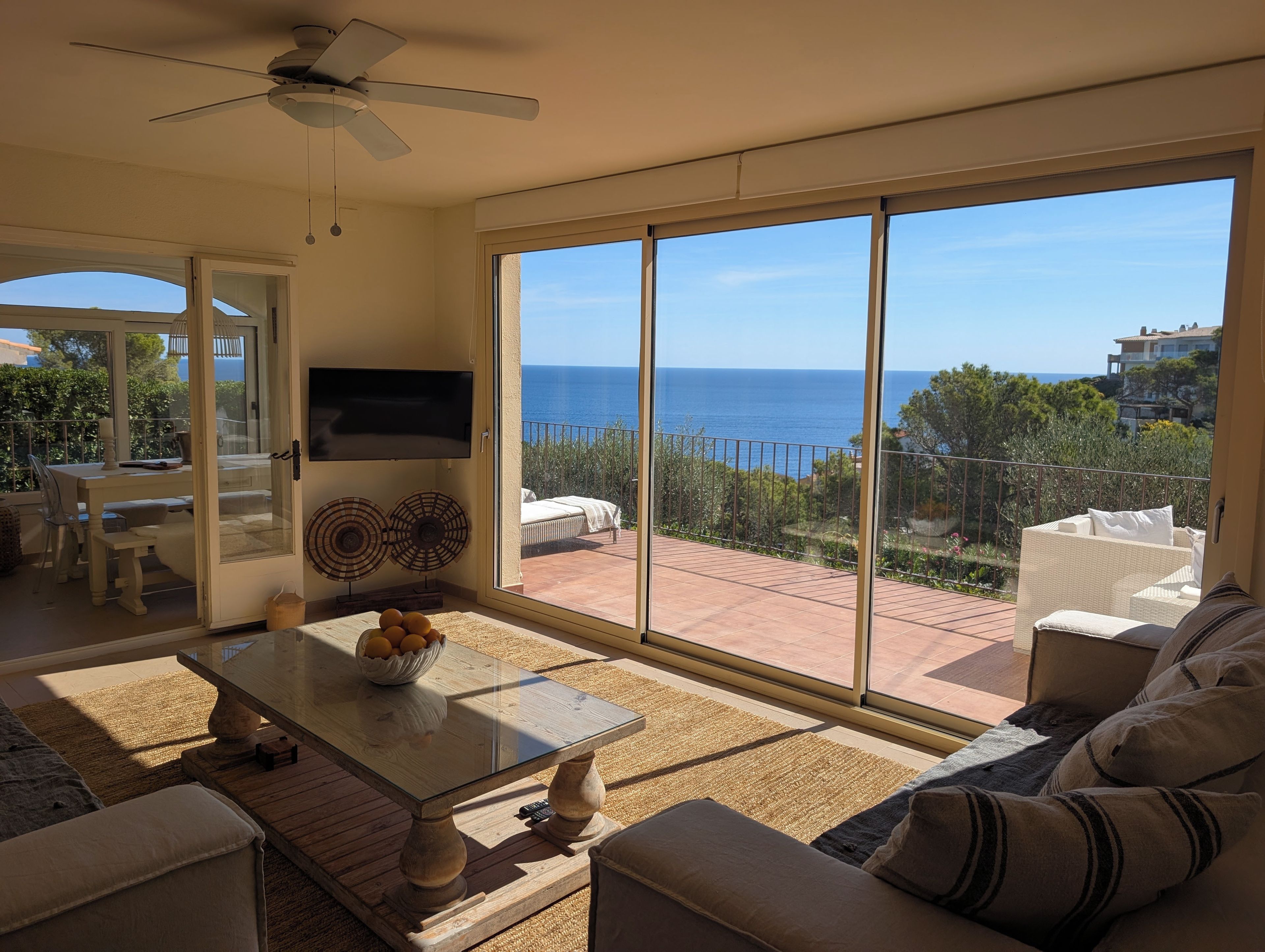 A spacious living room with a large sliding glass door leading to a balcony with a view of the sea.