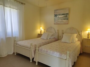 A double bed with a floral bedspread, two bedside tables with lamps, a painting on the wall, and a window with curtains. - Sea views, 2 Mins Walk to the Sea, Heated Pool, Air Con, Fibre WiFi, 90+ reviews (Aiguafreda, Begur)
