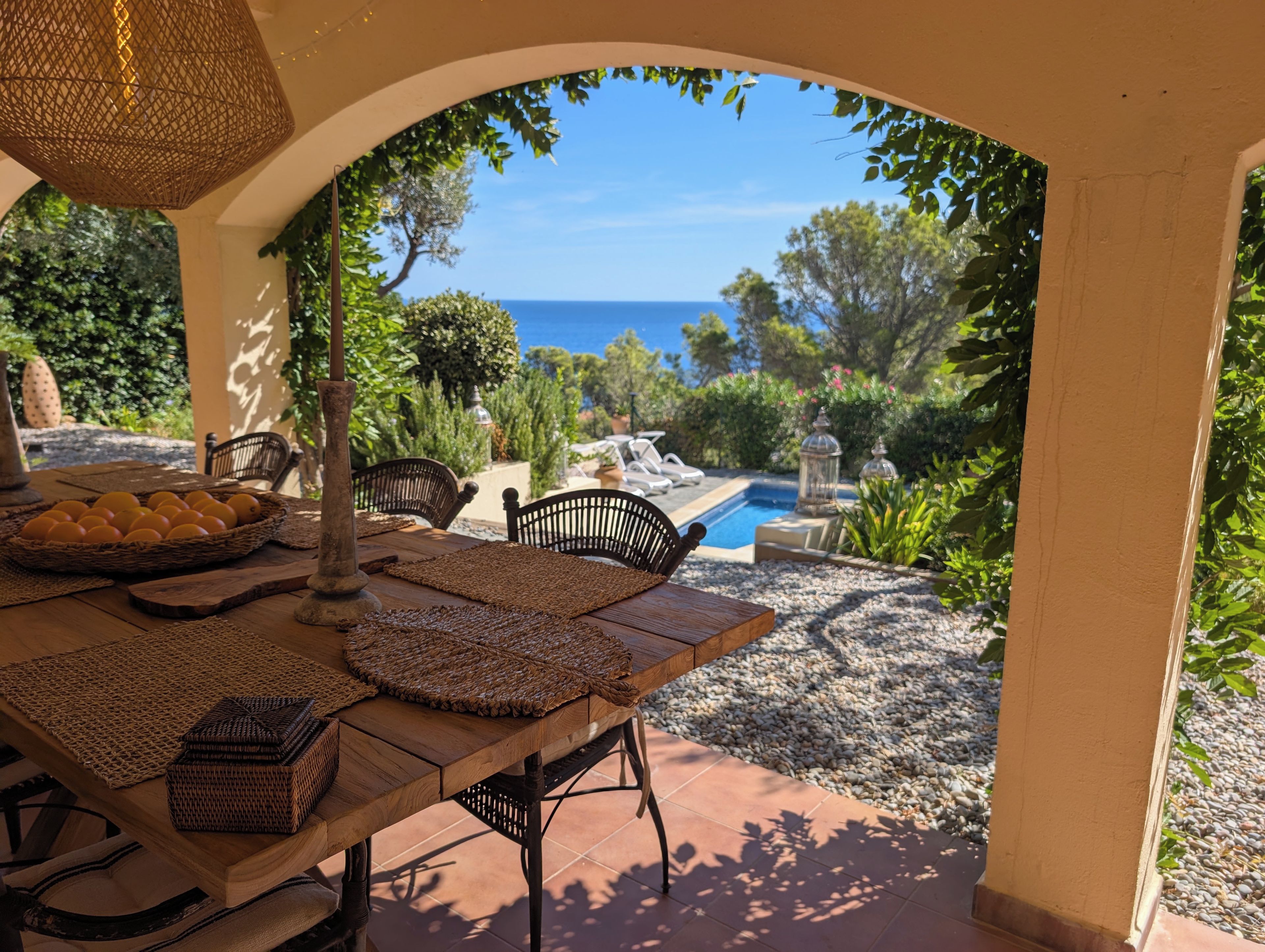 Un espace extérieur aménagé pour les repas, offrant une vue sur la mer, une piscine et la verdure environnante.