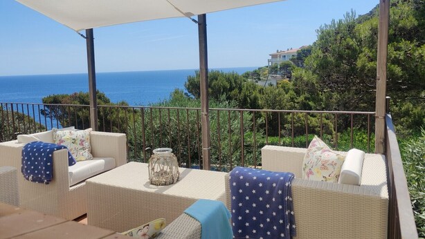 Un área de estar al aire libre techada con mobiliario de mimbre, una mesa y vista al mar.