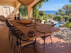 Zona pranzo all'aperto con tavolo in legno, sottopiatti intrecciati, sedie in vimini e vista sull'oceano.