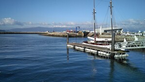 Una marina amb vaixells amarrats al moll, un far al fons i aigua tranquil·la.