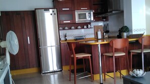 Cuina moderna amb frigorífic, microones i armaris de fusta. Hi ha una taula de menjador amb cadirees i una petita catifes al terra.