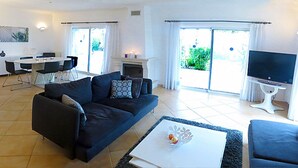 Ein modernes Wohnzimmer mit einer Couch, einem Couchtisch und einem Fernseher. Es gibt einen Essbereich mit Tisch und Stühlen.