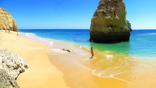 Ein Strand mit klarem türkisblauem Wasser, sandigem Ufer und großen Felsformationen.