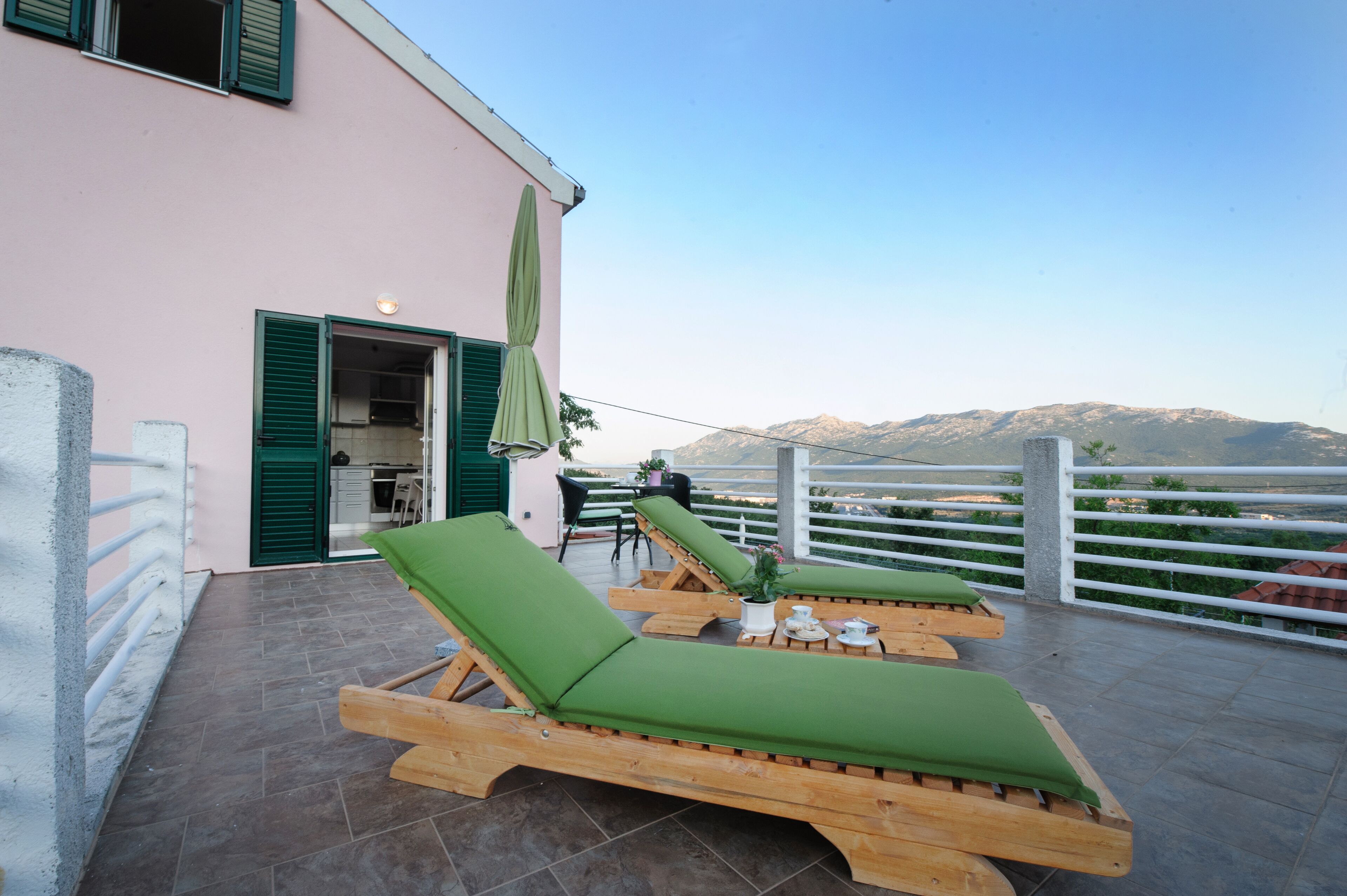 Une terrasse avec des fauteuils de jardin en bois et une table, un petit coin cuisine et une vue sur les montagnes.