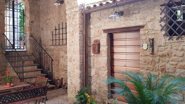 A rustic stone building with a wooden door, a staircase, and a table with chairs.