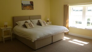 A bedroom with a large bed, two bedside tables, a painting on the wall, and a window with curtains. - Tastefully renovated, ideally located cottage for a peaceful or active break. (Cornhill-on-Tweed)