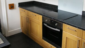 A kitchen with wooden cabinets, a black countertop, and a built-in oven. - Tastefully renovated, ideally located cottage for a peaceful or active break. (Cornhill-on-Tweed)