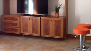 Un salon avec un téléviseur posé sur un meuble en bois, une plante en pot et un tabouret de bar.