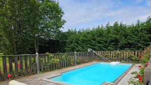 Une terrasse en bois avec une piscine, entourée d’une clôture en bois et d’une végétation luxuriante.